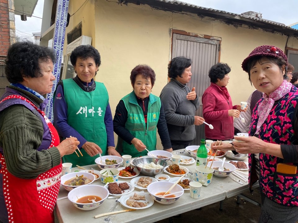 마당 테이블에 한상 차려놓고 식사를 하는 새마을회 회원들 모습.