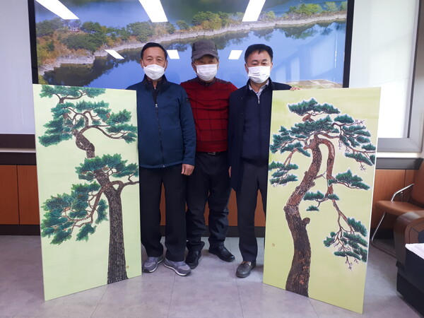  박찬훈 씨(가운데)가 군북면행정복지센터에 소나무 그림 2점을 기증하고 있다.