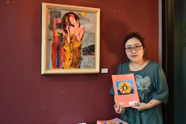 김경희 작가가 작품 앞에서 전시 도록을 들며 사진을 찍고 있다. 그는 선구적인 여성의 이미지를 다이아몬드와 결합해 다양한 색채로 표현했다.