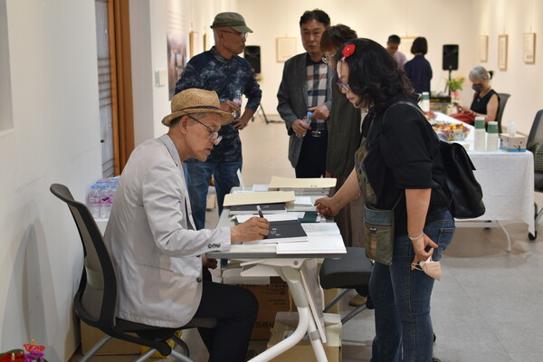 김성장(왼쪽) 씨가 전시 개막 행사를 찾은 손님들에게 싸인을 하고 있다.