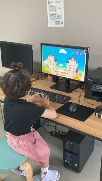 한 아이가 컴퓨터로 이론을 배우고 있다. 컴퓨터에 나와있는 것처럼 손을 따라하고 있다.