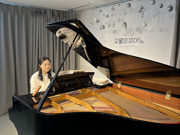 한혜경 대표가 진지한 표정으로 그랜드 피아노 앞에 앉아 피아노를 연주하고 있다.